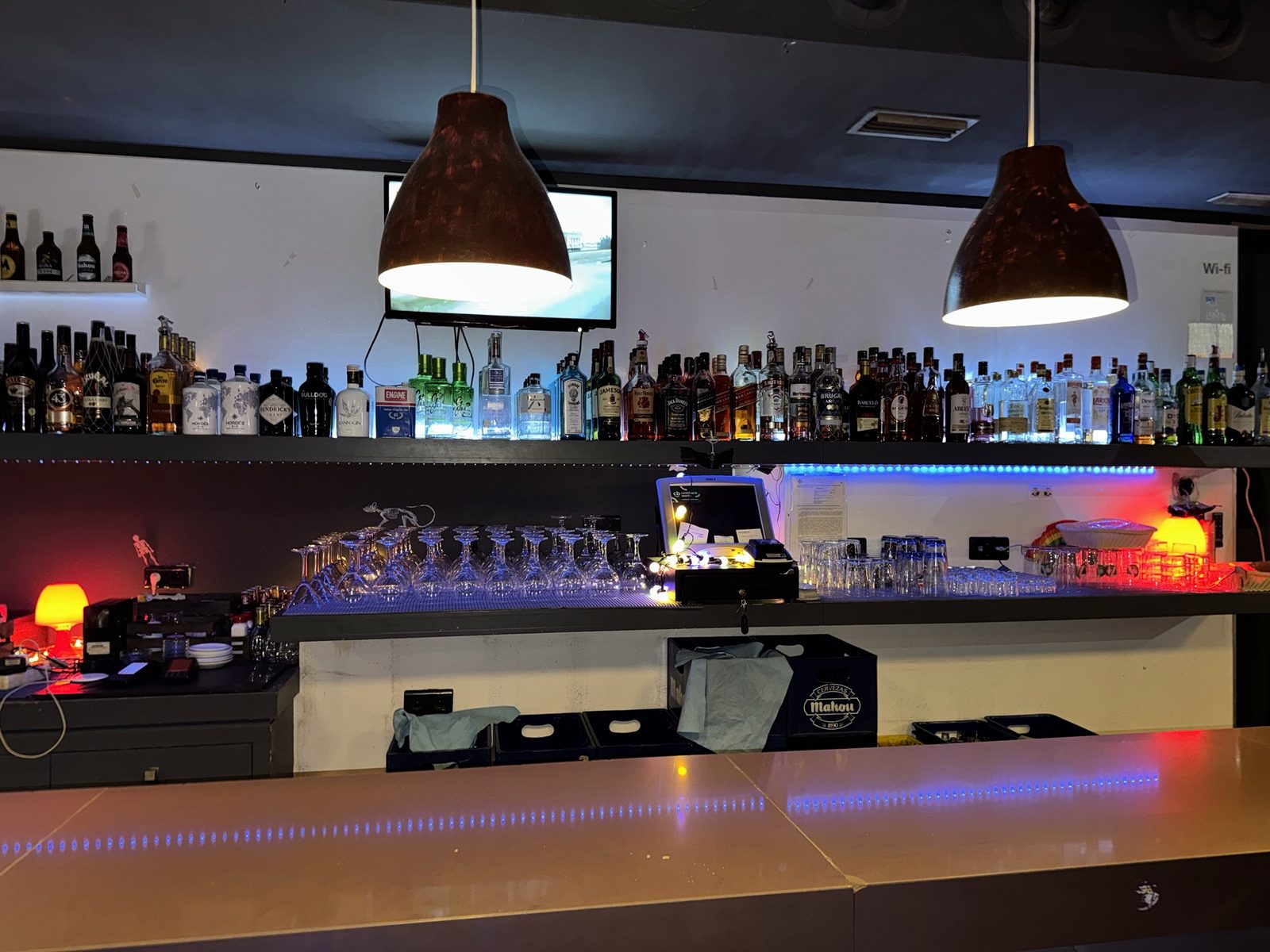 Barra del Raspabar con estantes llenos de botellas, lámparas colgantes y luces de colores