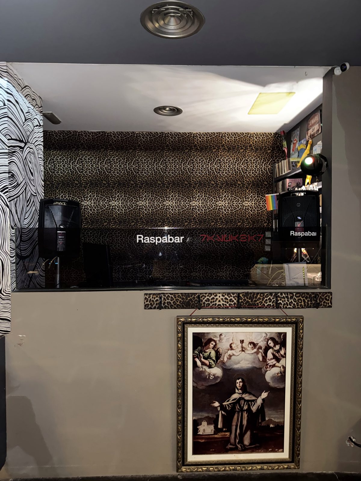 Cabina del Raspabar con fondo de leopardo, altavoces y un cuadro antiguo debajo