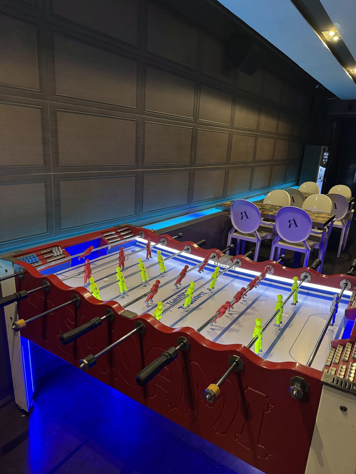 Futbolín con jugadores rojos y amarillos y luces de neón azul